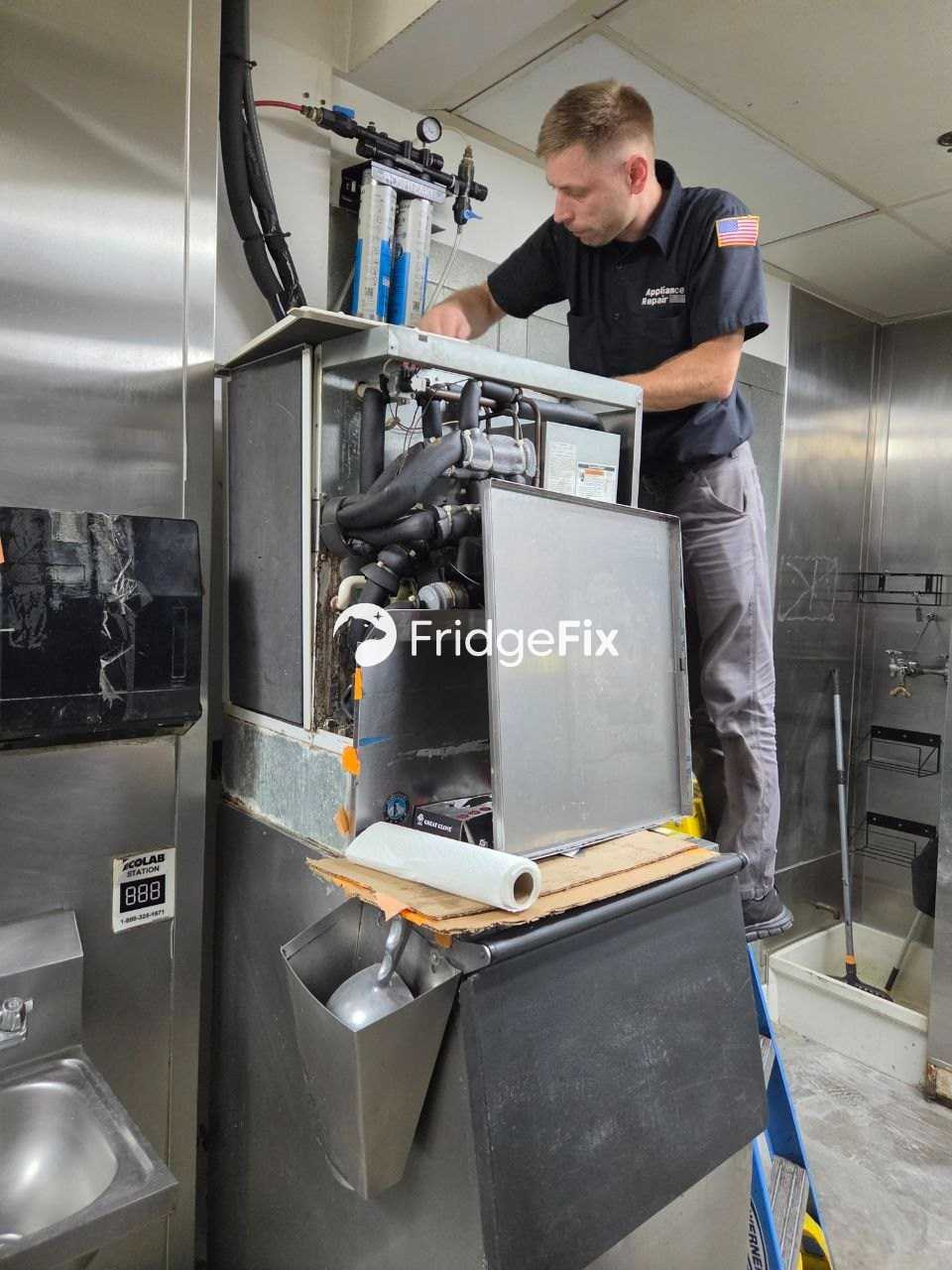 FridgeFix technician repairing a commercial ice machine in a restaurant kitchen