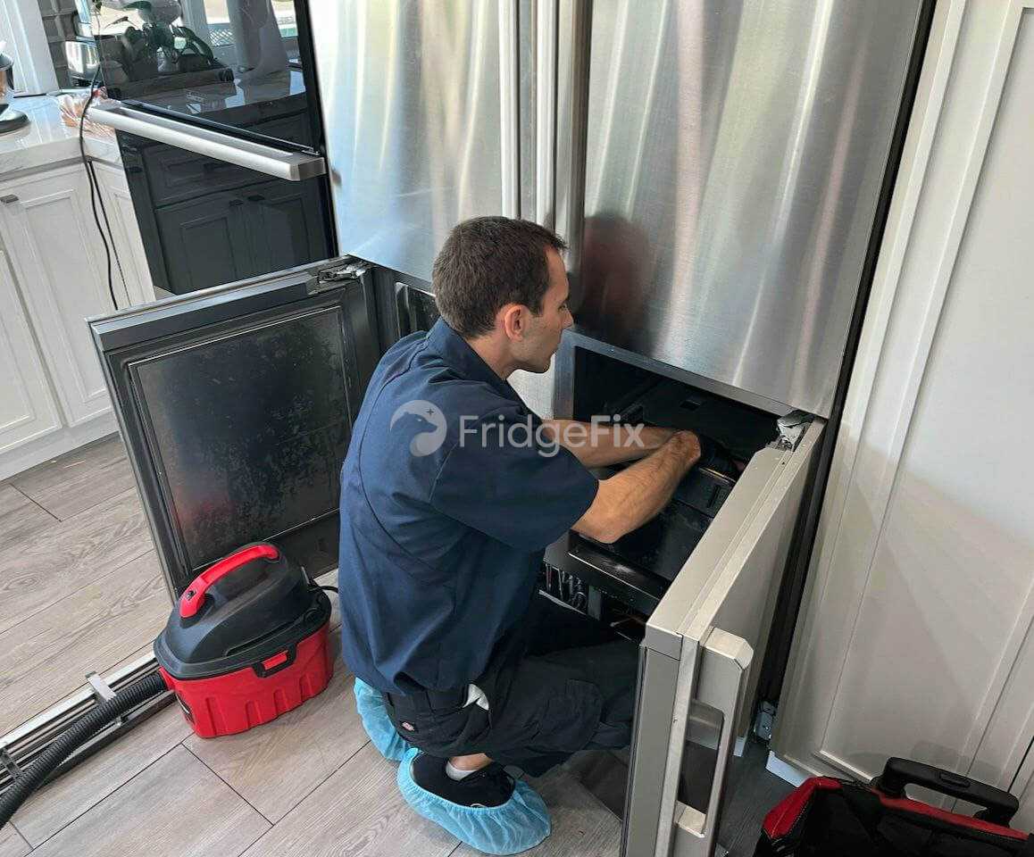 A man in a uniform diligently works on a refrigerator in a kitchen