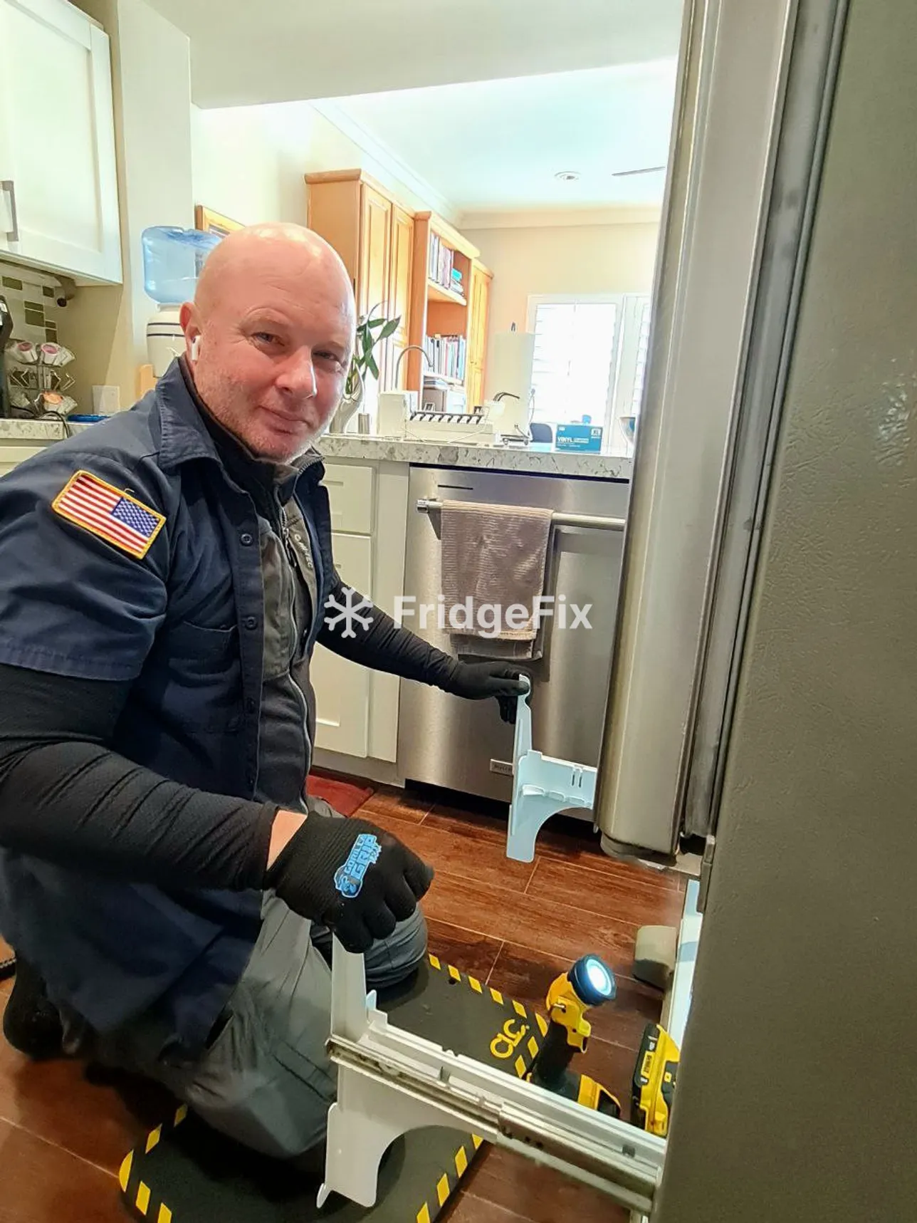 A technician in a blue shirt kneels before a refrigerator, inspecting its interior for repair needs